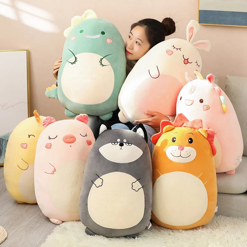 Woman holding and surrounded by a variety of large kawaii animal plush toys, including bunny, dinosaur, pig, raccoon, lion, and unicorn designs, displayed on a sofa.